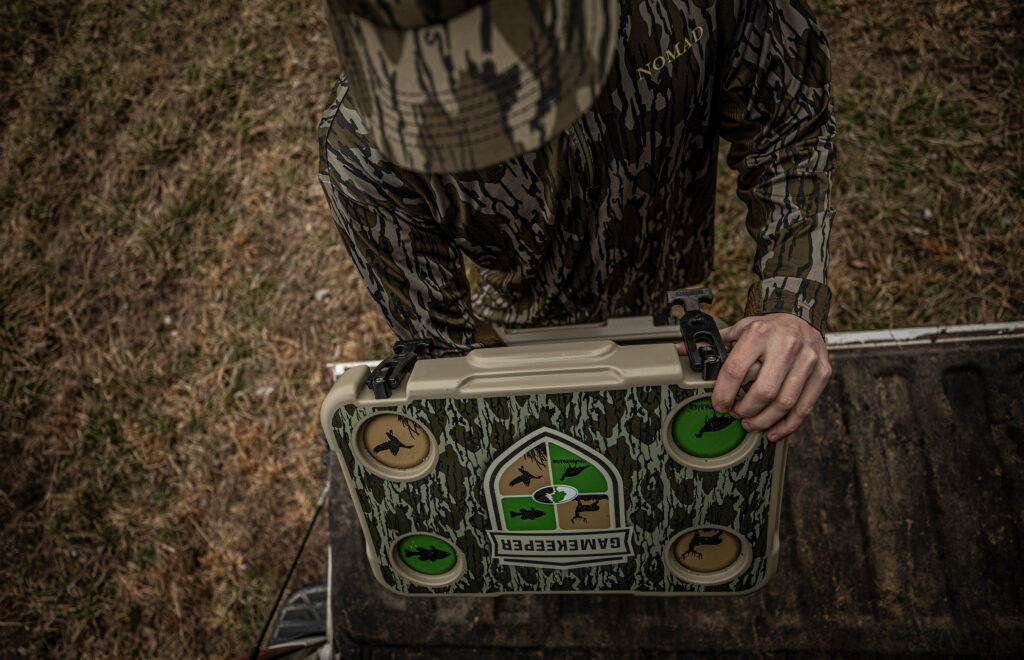 Hunter wearing camo opening their Mossy Oak Gamekeeper wrapped Mammoth Cooler